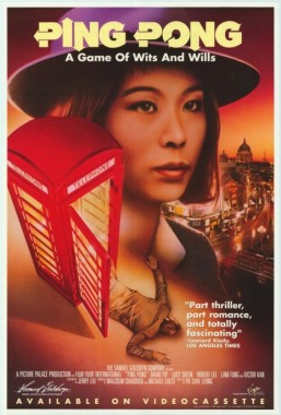 A cool young Chinese heritage woman in a Trilby stands near a red British phone box. A man's body lies on the ground, half inside the box.